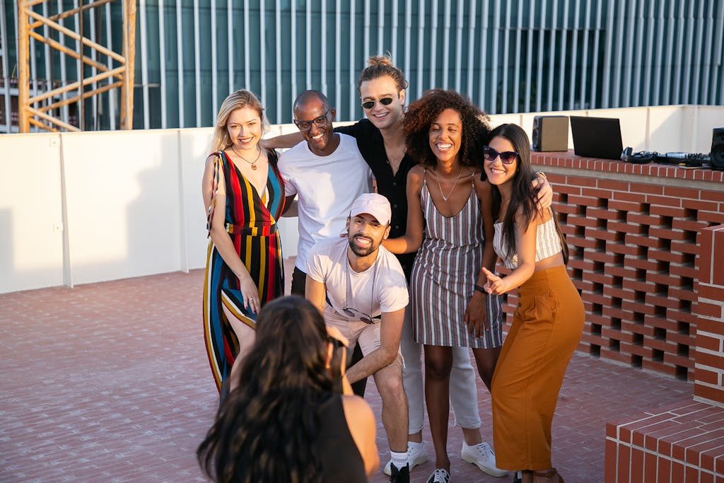 From above of anonymous lady taking photo of group of happy stylish multiracial friends chilling together on building terrace on sunny day