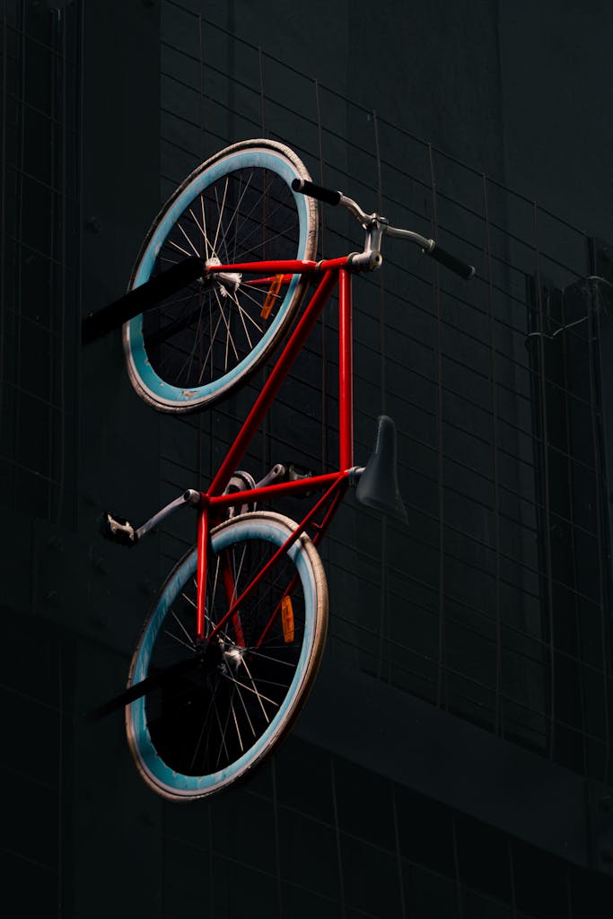 Red bicycle hanging on a dark urban wall, creating a striking contrast.
