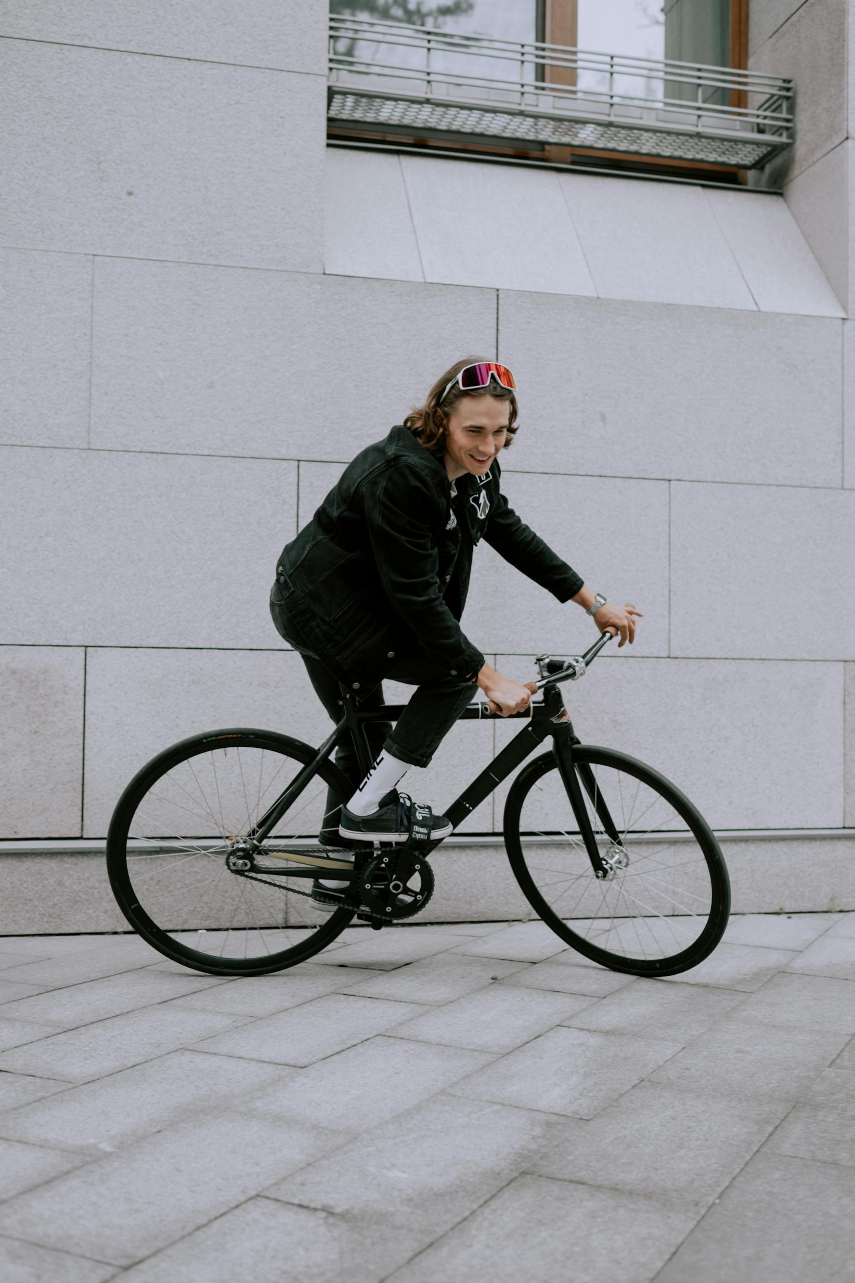 Young adult cycling on a fixie bike beside a modern building in an urban area.