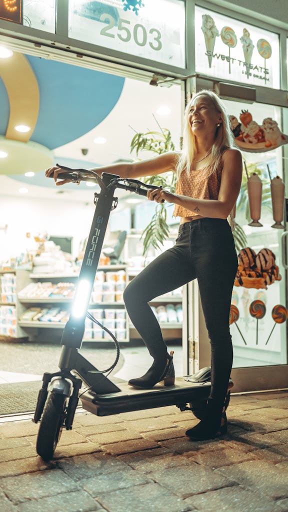 Young woman enjoys an evening urban ride on an electric scooter outside a city shop.