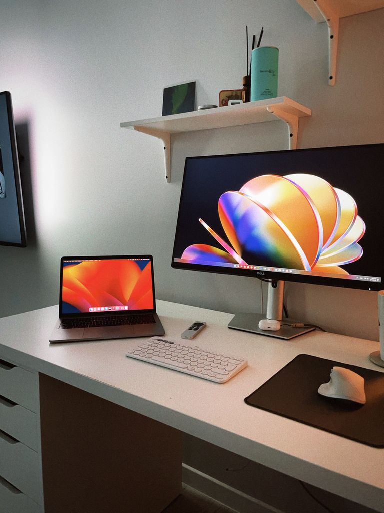Minimalist office setup featuring a laptop and large monitor on a white desk.
